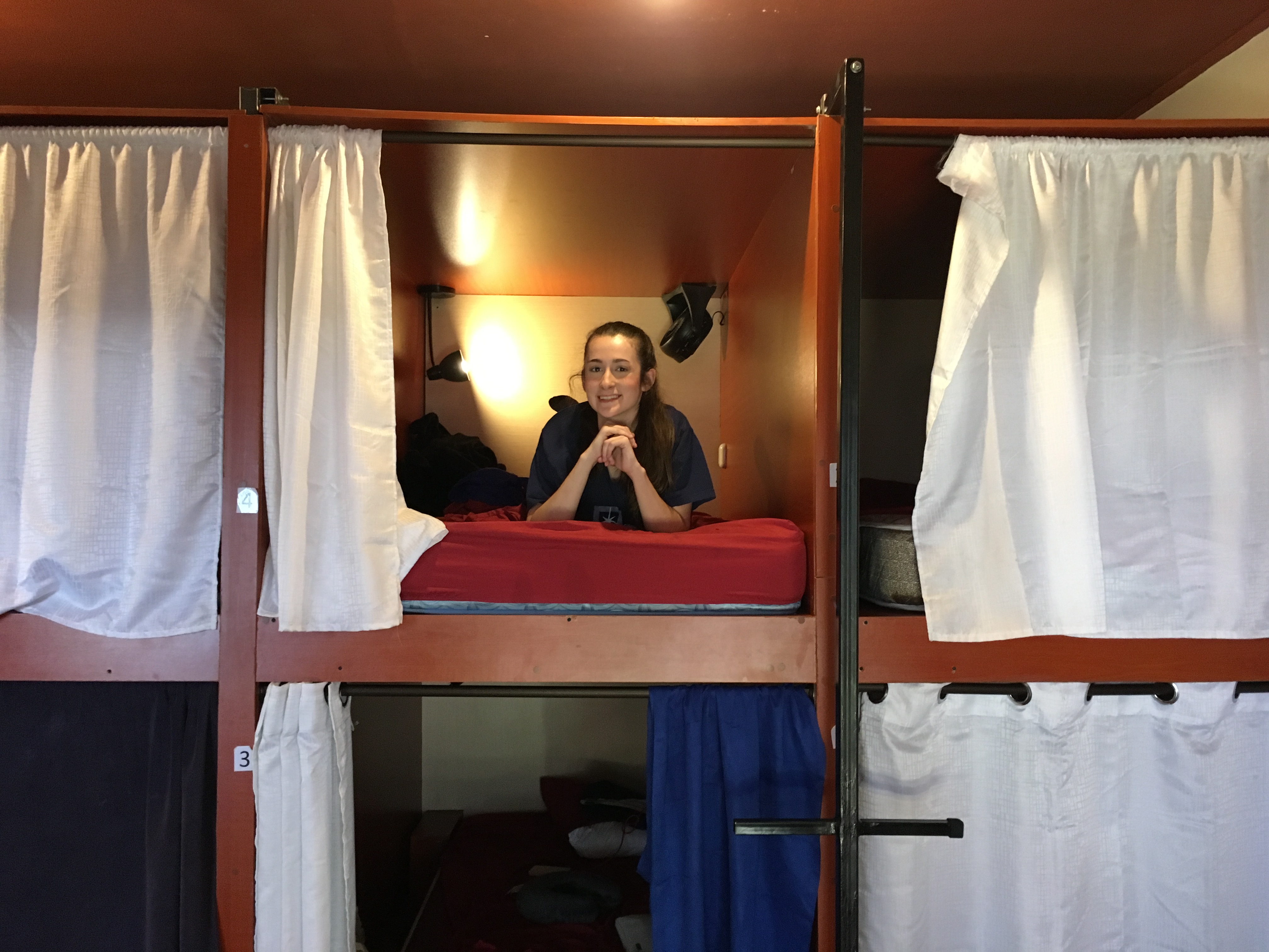 A woman sits on one of the capsule beds in her hostel. 